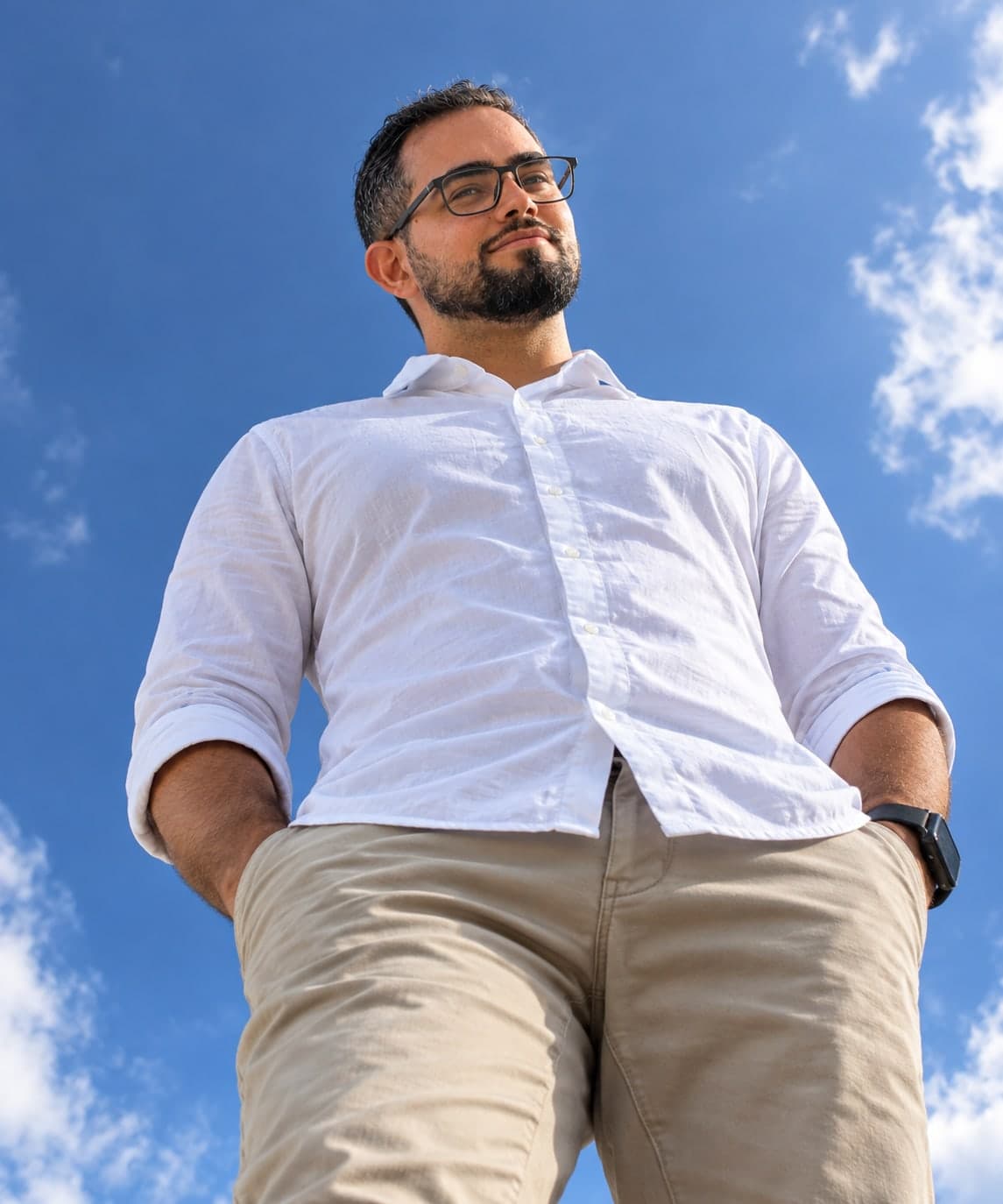 Felipe Amorim in glasses and a white shirt, photographed from below against a blue sky