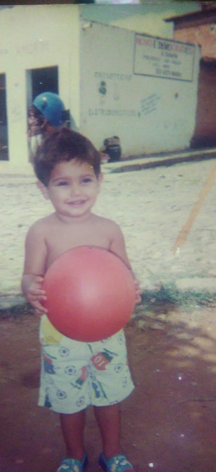 Felipe criança sorrindo, segurando uma bola vermelha na rua