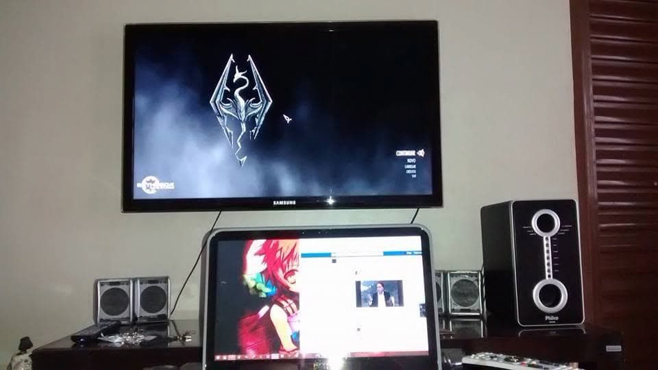 Setup com TV mostrando Skyrim, computador e caixas de som